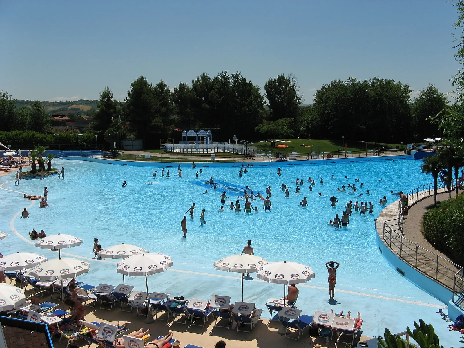 La grande piscina di Aquafan a Riccione con ombrelloni e lettini; bagnanti piccoli e lontani.