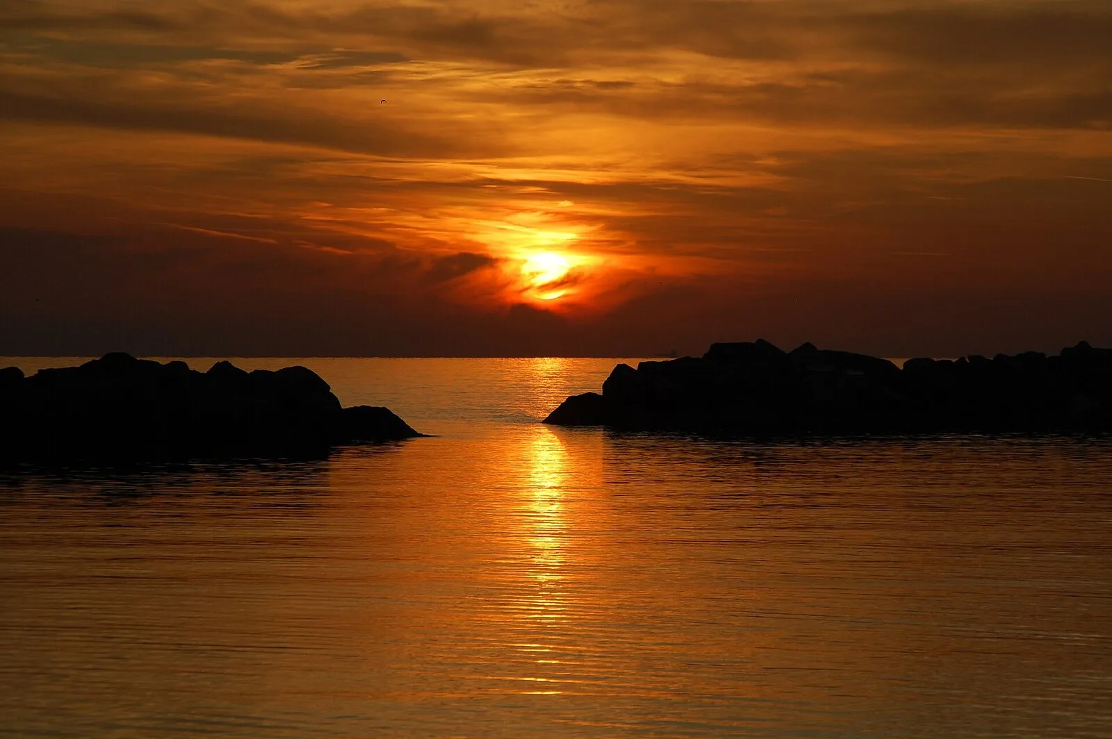 Sonnenaufgang über dem Meer bei Bellaria Igea Marina: Die Sonne geht zwischen den Wellenbrechern auf und spiegelt sich im Wasser