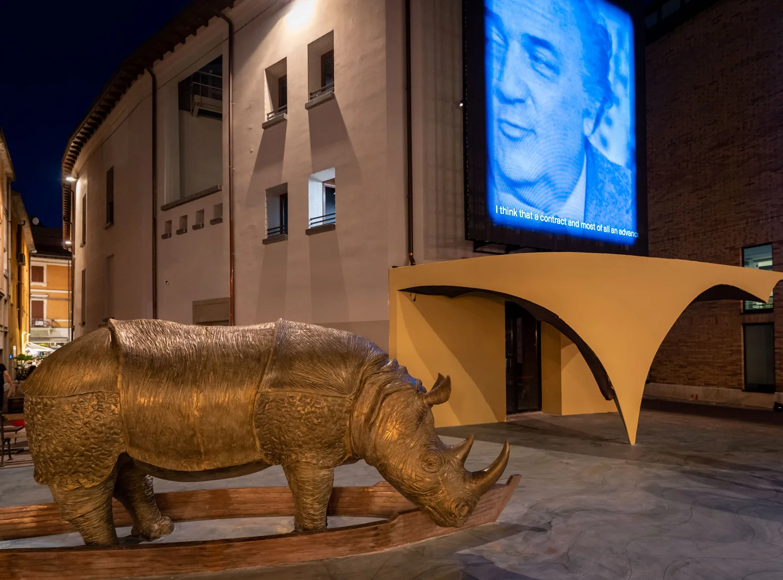 Die Piazza Malatesta am Abend mit dem goldenen Nashorn und dem Gesicht von Federico Fellini auf der großen Leinwand des Fellini Museum