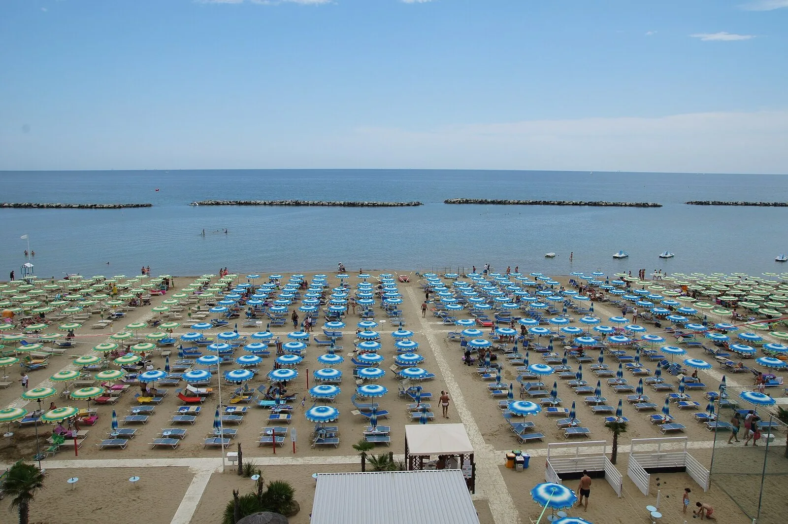 Der Strand von Igea Marina von oben, mit Reihen von Sonnenschirmen, ruhigem Meer und den Wellenbrechern vor der Küste
