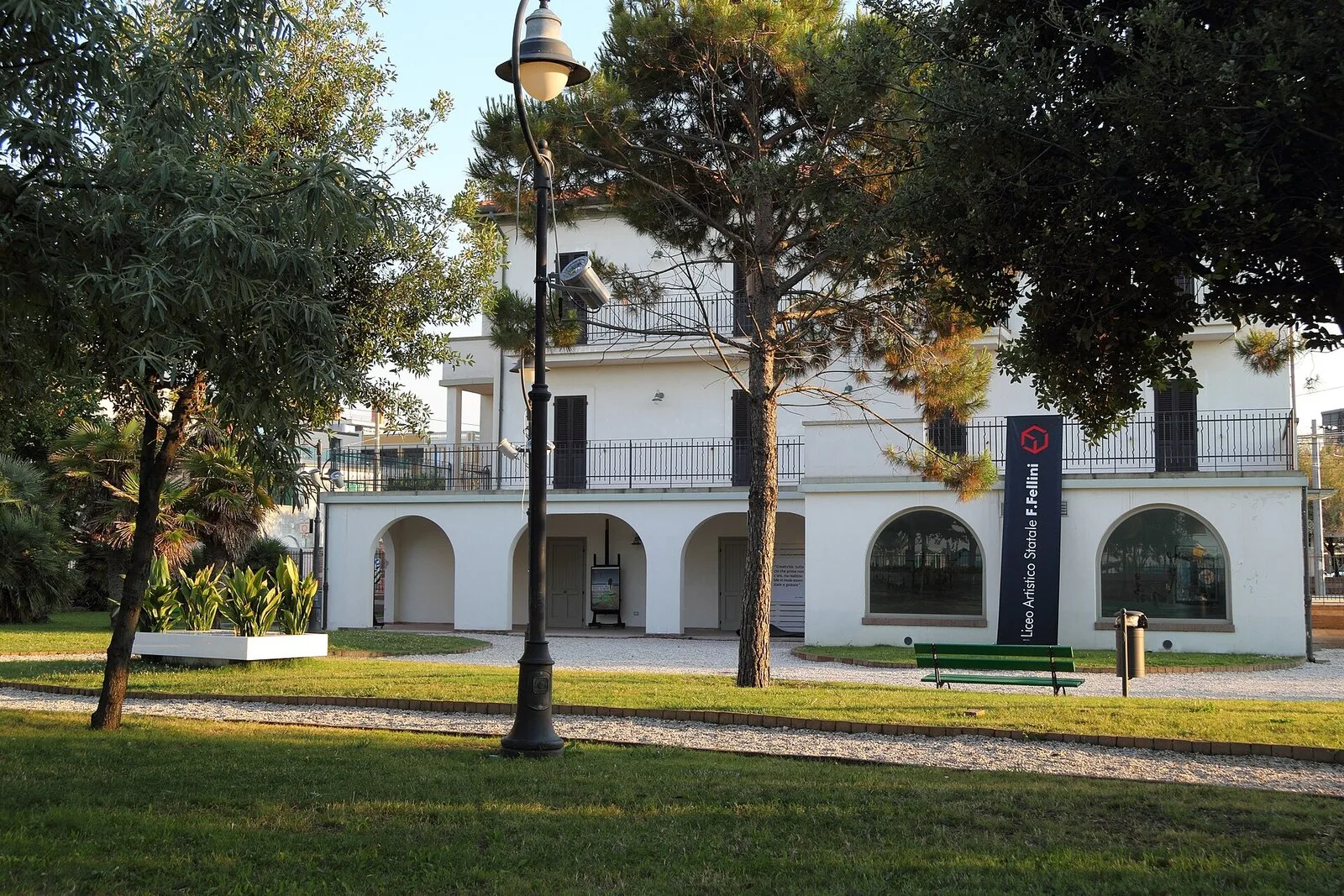 Villa Mussolini a Riccione, edificio bianco con portico ad archi, visto dal parco con prato e pini