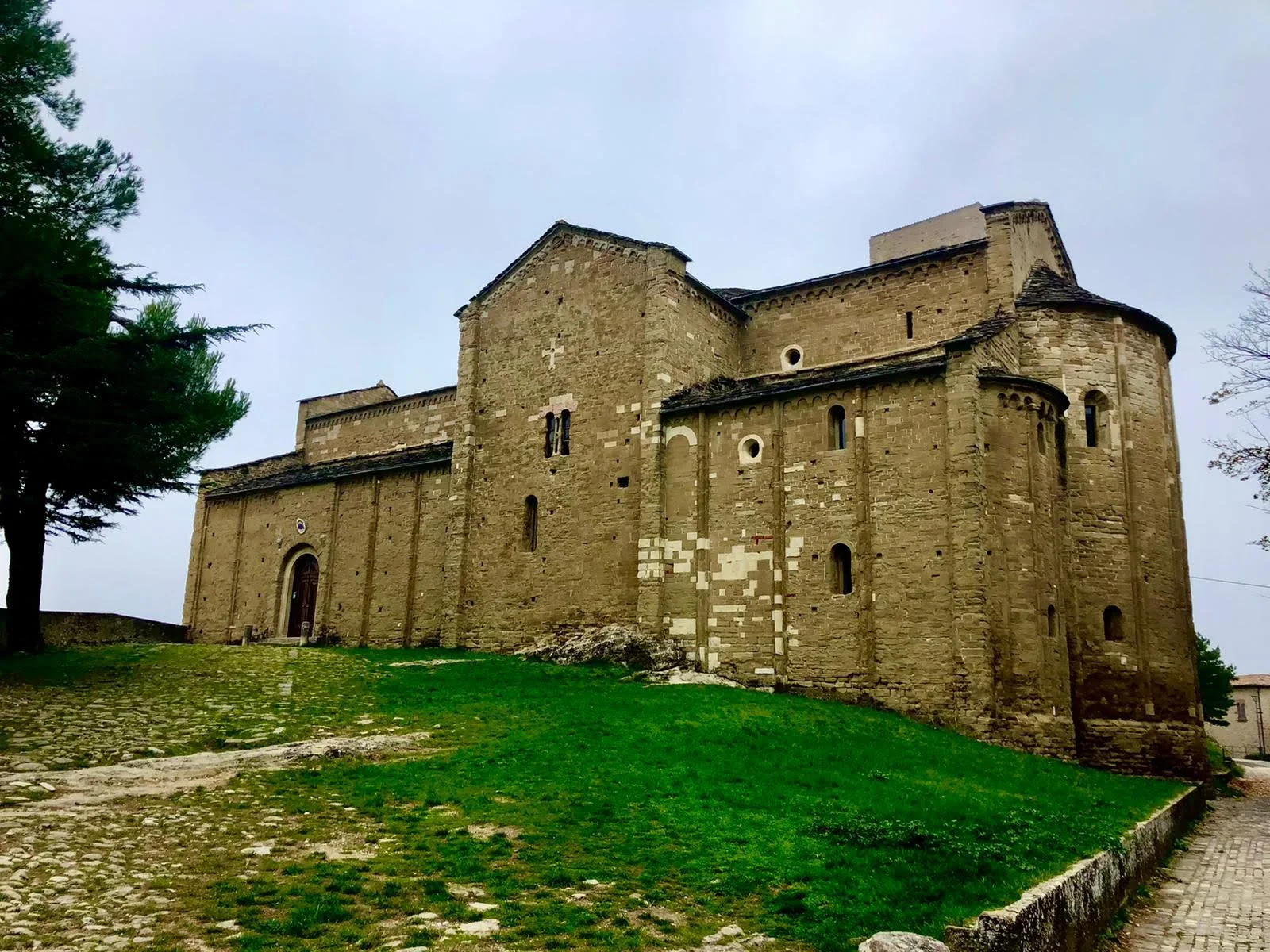 Der romanische Dom von San Leo aus Sandstein, mit den Apsiden und der Wiese davor