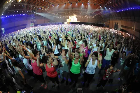 Migliaia di partecipanti a braccia alzate durante una lezione di fitness collettiva in un padiglione della Fiera di Rimini a RiminiWellness