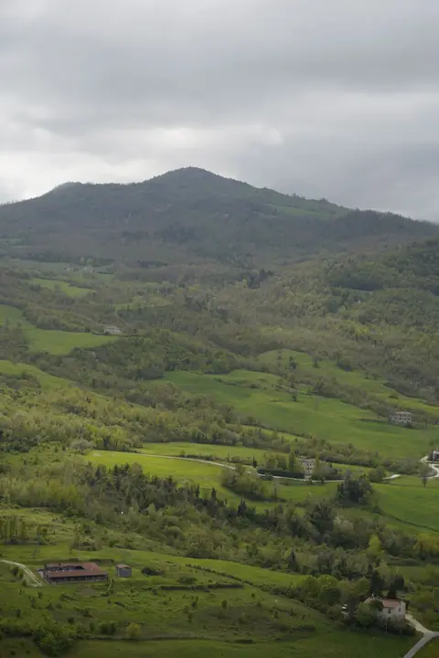Le colline verdi intorno a San Leo in primavera, con prati, boschi e case coloniche del Montefeltro