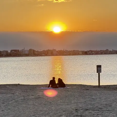 Una coppia seduta sulla spiaggia guarda il tramonto sul mare della Riviera di Rimini