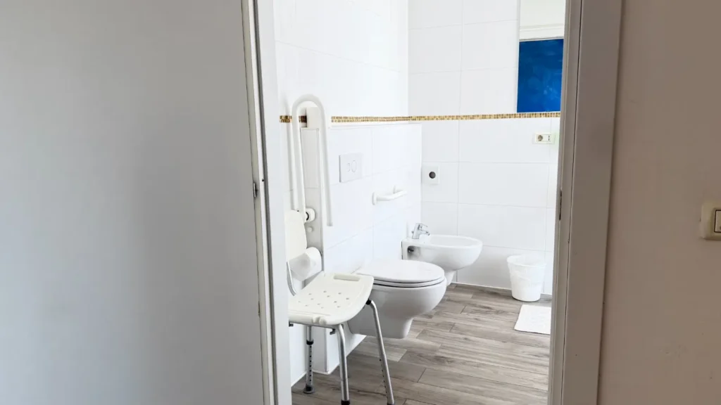 Bagno per disabili dell'Hotel Viking con maniglione ribaltabile e maniglione fisso accanto al WC e seggiolino per la doccia