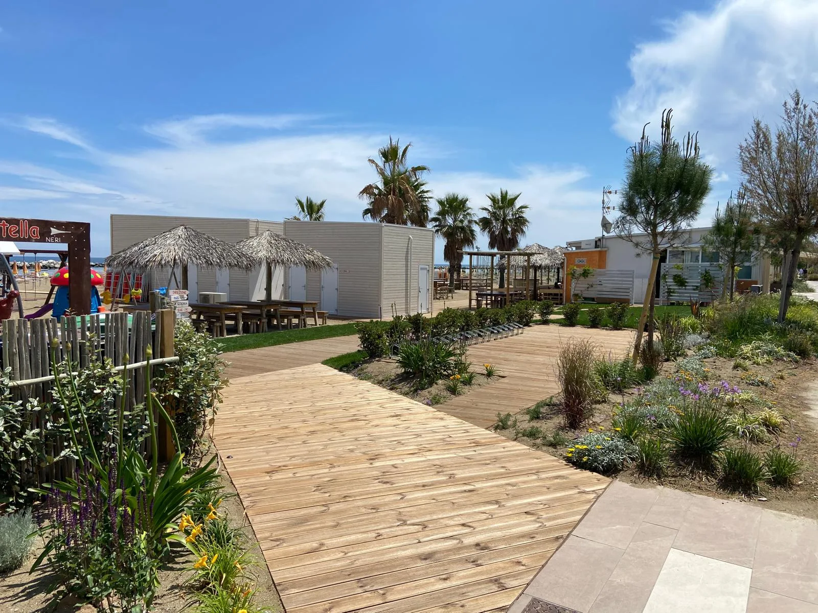 Passerella in legno, giardino fiorito e area giochi per bambini al Bagno 53 Neri di Viserbella