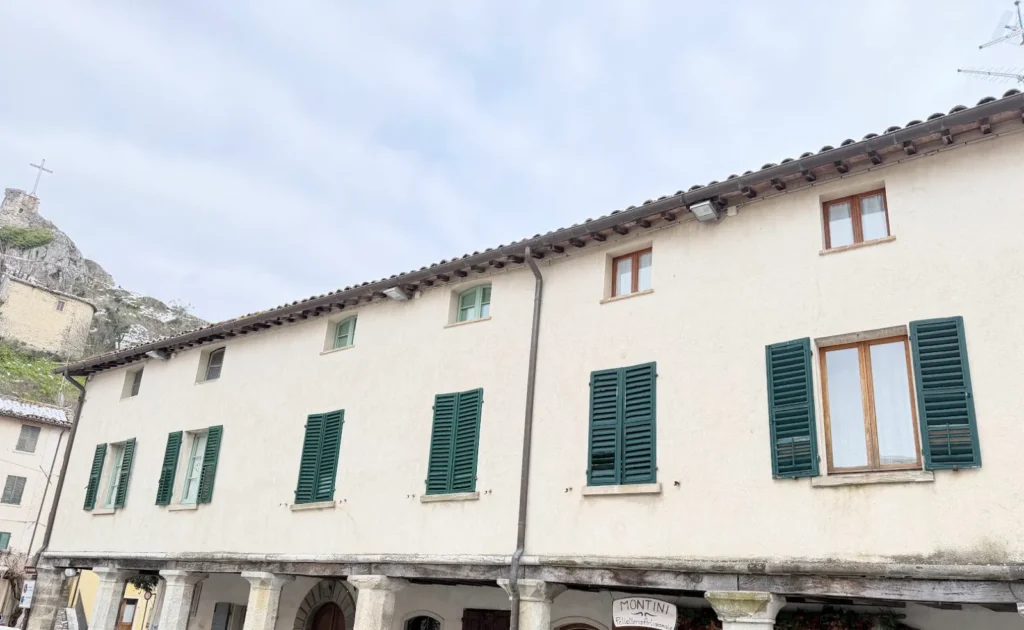 Palazzo con portico in pietra e persiane verdi nel centro storico di Pennabilli, con il Roccione sullo sfondo
