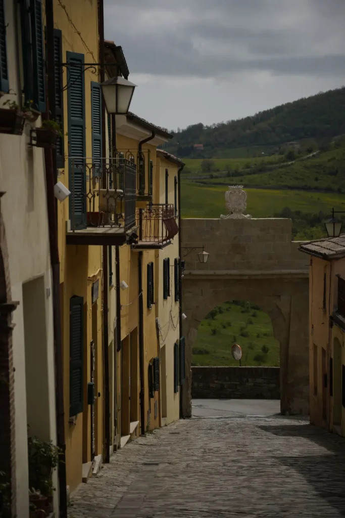 Vicolo acciottolato del borgo di San Leo con la porta d'ingresso in pietra e le colline del Montefeltro