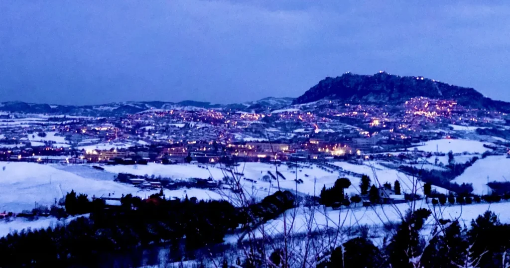 Il Monte Titano e San Marino illuminati di sera, con le colline coperte di neve